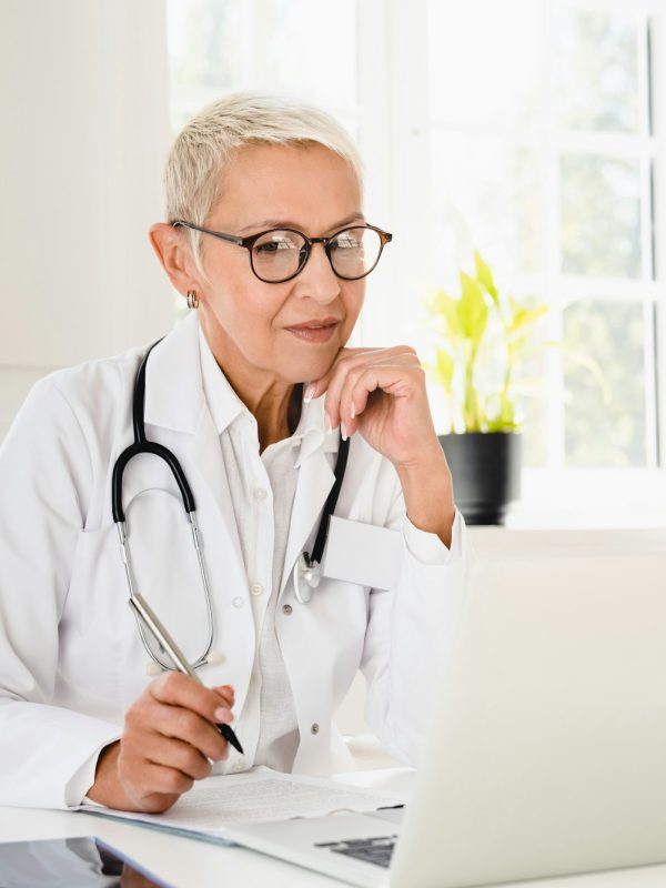 Doctor in white coat working on laptop, looking for diagnosis, telemedicine with patient at hospital